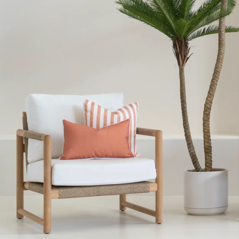 A wooden single-seater sofa styled with two rust outdoor cushions.