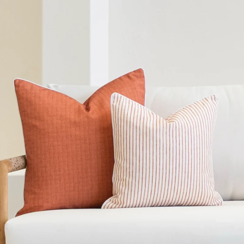 Corner of a white sofa with a set of 2 pacific rust outdoor cushions sitting on it.