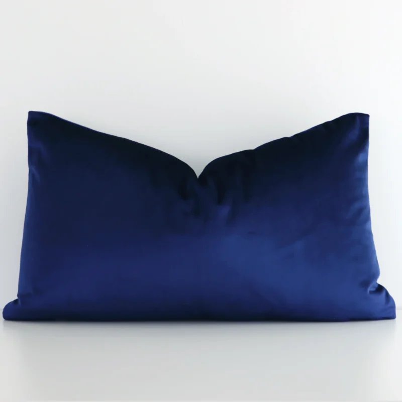 Royal blue cushion cover in front of a white wall. It has a rectangle size and is made from a velvet material.