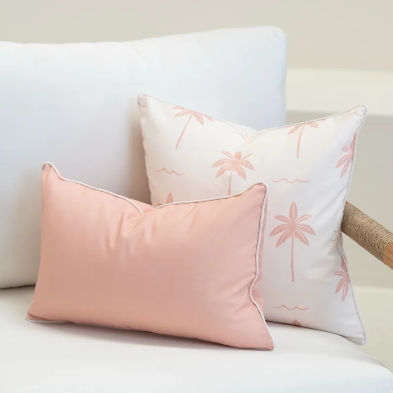 Tropica pink cushions with palm print paired with solid blush rectangular cushion on sofa.