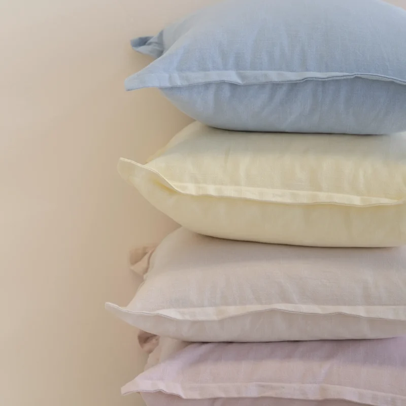 Close-up of stacked linen cushions showing soft pastel colours and textured fabric.