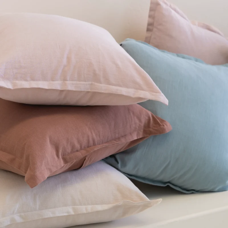 Close-up of stacked linen cushions showing blush, rust and pale blue textures.