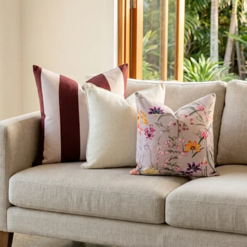 Three-piece cushion set with a mulberry striped cushion, a cream cushion, and a vivid floral print, on a couch.