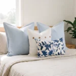Four-piece cushion set with two sky blue linen blocks, a white button cushion, and a lily print lumbar, on a bed.