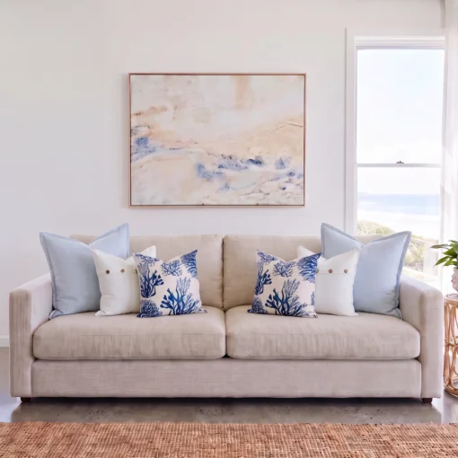 Six-piece cushion set with matching sky blue linen, white button, and coral print cushions, on a sofa.