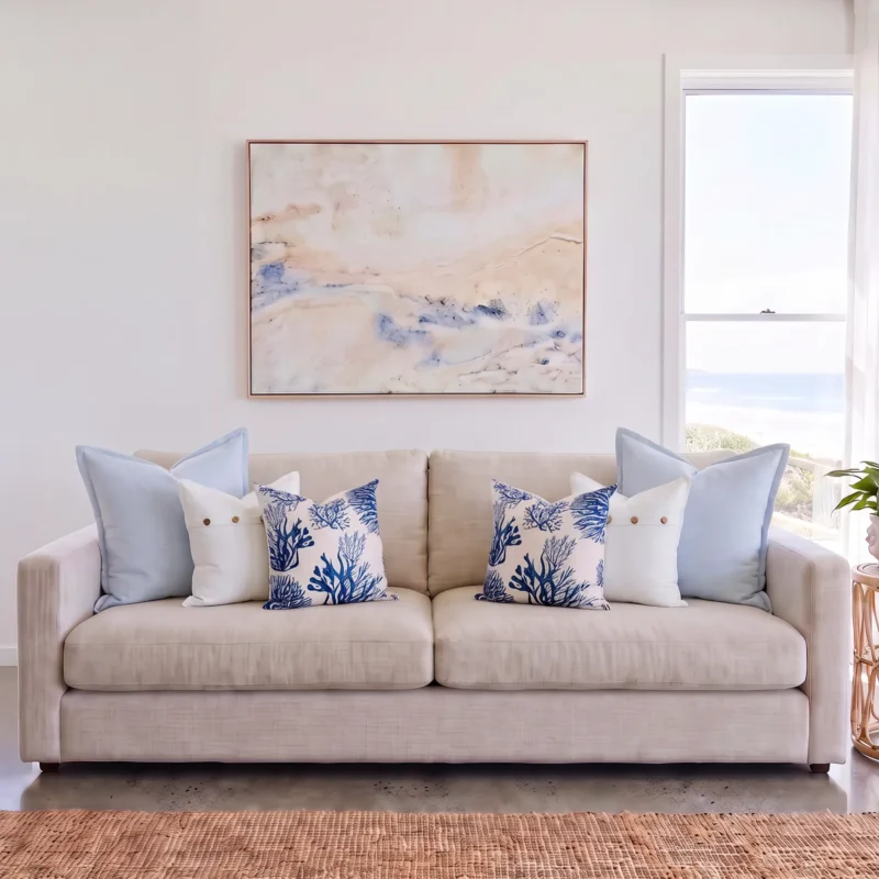 Six-piece cushion set with matching sky blue linen, white button, and coral print cushions, on a sofa.