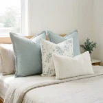 Four-piece cushion set with two sage blocks, a botanical print, and a white boucle lumbar, on a bed.