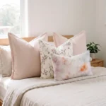 Four-piece cushion set with two blush linen blocks, a botanical print, and a watercolour lumbar, on a bed.