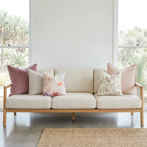 Five-piece cushion set with blush linen and velvet blocks, floral and watercolour prints, and a striped accent, on a sofa.